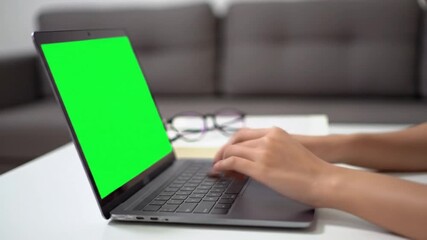 Person typing on a laptop with a green screen on a table.