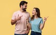 © yuan - Portrait of content surprised couple man and woman in basic t-shirts pointing fingers upward at copyspace with open mouthes. High quality