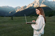 © SHOTPRIME STUDIO - A focused outdoor professional uses a laptop in a scenic mountain meadow. She stands with calm concentration, blending technology with nature to create a serene and productive work setting.