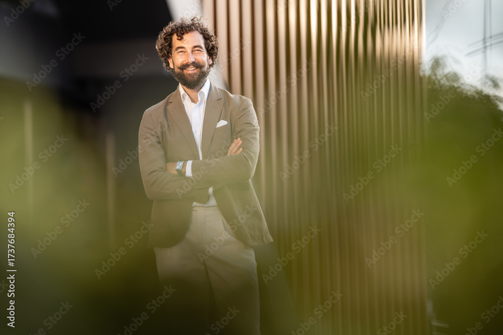Smiling businessman with crossed arms posing in front of modern ...