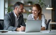© Joseph - Mature focused senior mentor leader man showing young woman manager project on laptop in modern office. Two partners, team of professional business people working, studying, writing notes sit at desk