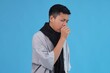 © Gatot - Asian Kid Coughing into His Hand, Feeling Unwell and Sick Against Vibrant Blue Background