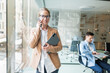 © muse studio - Businesswoman talking on phone in modern office with colleague