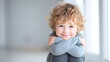 © utaem2022 - Young child with curly hair sitting on floor, smiling warmly in bright indoor environment