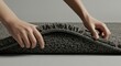© Zhanna - Hands rolling up a plush gray rug on a neutral background