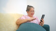 © Wosunan - On a holiday, an elderly woman relaxes with a smartphone on the sofa