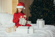 © polinaloves - Cute 7-years old girl wearing Santa hat and holiday pajamas enjoying her a Christmas presents in a festive bedroom.