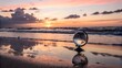 © Natalia - A glass globe rests on a sandy beach at sunset. Waves gently lap at the shore, reflecting the vibrant colors of the sky. The scene conveys a sense of tranquility and exploration.