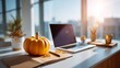 © O - Orange pumpkin on office desk with laptop. Autumn season at modern workplace. Fall business concept with sunlight.