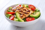 Grilled chicken salad with avocado and tomatoes in a white bowl on a light background, top view, flat lay. Healthy food idea. Concept for healthy eating, weight loss, or body-building advertising