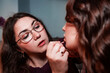 © fotodiya83 - Make-up artist paints the lips of a client. Makeup artist applying make up to a beautiful young woman in a professional salon. Beauty, fashion and skin care industry. Work. Lipstick, lip gloss.
