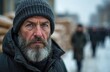© Vadym - Mature man with grey beard wears warm winter hat and dark coat. He has blue eyes and stern expression. People queue in blurred city background on cold day, waiting for aid and help.