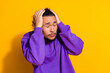 © deagreez - Confident young man in a purple hoodie with a vibrant yellow background posing with hands on head, casual style
