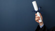 © photo for everything - Graduation success! Celebratory image of a graduate holding a diploma tied with a navy blue ribbon against a dark blue background.
