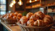 © Viktor - Fresh croissants lie in baskets inside local bakery shop. Warm cozy light falls on pastries. Food concept showcases bread assortment on shelves behind. Focus on foreground tasty viennoiseries.