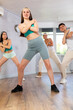 © JackF - Positive smiling female teenager learns dance hip hop, perform movements in choreographic class in company of peers. Young girls in ball cap and guy repeat movements, train in spacious studio