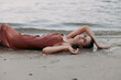 © SHOTPRIME STUDIO - A woman lies on a sandy beach in a flowing dress, arms stretched beside her, soft light, gentle waves, creating a serene and intimate mood on shore.