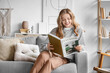 © Pixel-Shot - Beautiful young happy woman reading magazine while sitting on sofa at home