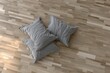 © Alfath - Three gray pillows rest on a light-colored hardwood floor, soft light from above