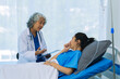 © ArLawKa - Elderly female doctor and Asian female patient are discussing something while sitting on hospital bed. Medical consultation concept.