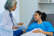 © ArLawKa - Elderly female doctor and Asian female patient are discussing something while sitting on hospital bed. Medical consultation concept.