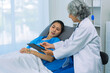 © ArLawKa - Elderly female doctor and Asian female patient are discussing something while sitting on hospital bed. Medical consultation concept.