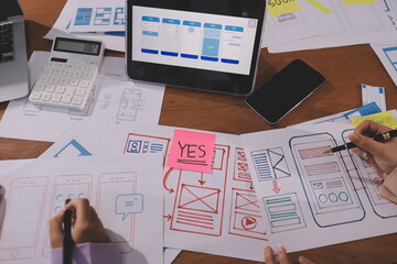 Close up ux developer and ui designer brainstorming about mobile app interface wireframe design on table with customer breif and color code at modern office.Creative digital development agency.