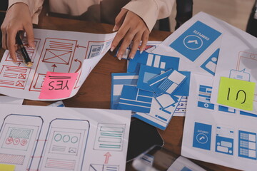 Close up ux developer and ui designer brainstorming about mobile app interface wireframe design on table with customer breif and color code at modern office.Creative digital development agency.