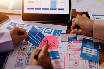 Close up ux developer and ui designer brainstorming about mobile app interface wireframe design on table with customer breif and color code at modern office.Creative digital development agency.