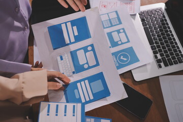 Close up ux developer and ui designer brainstorming about mobile app interface wireframe design on table with customer breif and color code at modern office.Creative digital development agency.