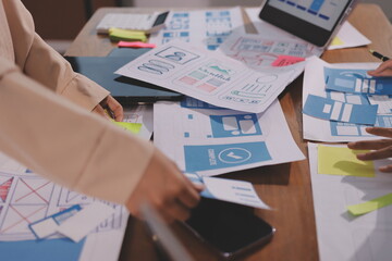 Close up ux developer and ui designer brainstorming about mobile app interface wireframe design on table with customer breif and color code at modern office.Creative digital development agency.