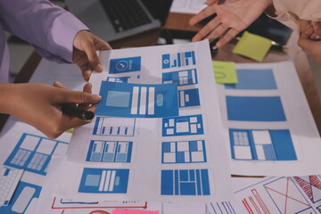 Close up ux developer and ui designer brainstorming about mobile app interface wireframe design on table with customer breif and color code at modern office.Creative digital development agency.