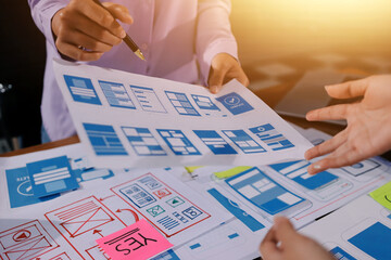 Close up ux developer and ui designer brainstorming about mobile app interface wireframe design on table with customer breif and color code at modern office.Creative digital development agency.