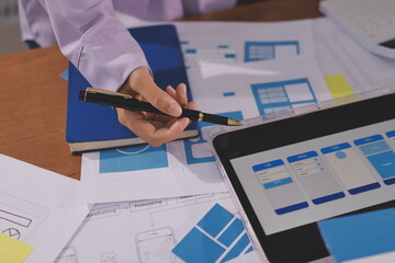 Close up ux developer and ui designer brainstorming about mobile app interface wireframe design on table with customer breif and color code at modern office.Creative digital development agency.