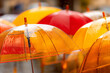 © Alexander - Close-up of colorful transparent umbrellas with raindrops overlapping in a rainy outdoor scene. Bright orange and red domes create reflective patterns and vibrant wet texture.