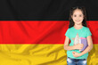 © New Africa - Little girl with notebooks against flag of Germany. Language school