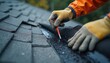 © Pete - Worker in protective gloves applies black waterproof sealant to house roof valley. Important work ensures residential home protection, preventing water leaks, improving overall building durability,