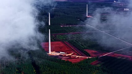 Wall Mural - Time-lapse aerial of wind turbine towers rising among dense forests and red soil fields in Latvia. Latvia