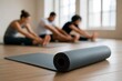 © hobonski - A rolled black yoga mat rests sharply on warm wooden floors as a blurred group stretches in unison  evoking calm, mindfulness, and collective wellness in a serene studio space.