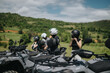 © qunica.com - Four people secure their helmets while standing beside quad bikes, surrounded by stunning green landscapes.