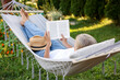 © New Africa - Senior woman reading book in hammock outdoors