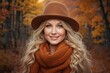 © The 2R Artificiality - Blonde woman wearing a brown hat and an orange scarf smiling in a vibrant autumn forest with colorful foliage in soft natural light.