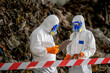 © BESTIMAGE - Two scientists in full protective suits working outdoors with clipboard and safety gear in a dangerous environment, ash and debris around them, inspection scene