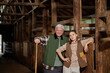 © Seventyfour - Caucasian senior man and Caucasian young adult woman standing together in rustic barn, both smiling and leaning on wooden railing, showing generational connection in agricultural setting