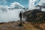 Kobieta stojąca na szczycie góry i podziwiająca panoramę gór i chmur, wędrówka wśród natury z poczuciem wolności i inspiracji