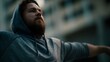 © Bussakon - A man with a beard in a grey hoodie stretches his arms outdoors in an urban setting looking upwards with determination