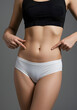 © Roman Stock studio - Woman pointing at her abdomen in activewear on grey background