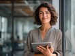 © saidul - Smiling young Hispanic professional business woman using tablet standing in office. Happy businesswoman manager, female executive leader holding tab at work, looking at camera. Portrait