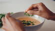 © Naret - Hands placing parsley garnish on creamy soup bowl, close up macro detail showing fresh herb adding flavor and color to meal