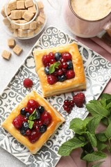 Wall Mural - Tasty puff pastries with berries, mint, brown sugar and coffee on light grey table, flat lay